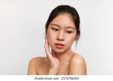 Essential Beauty Concept. Young Chinese Lady Touching Her Smooth Skin, Attractive Asian Woman With Dark Hair Looking Away, Posing Over White Studio Background