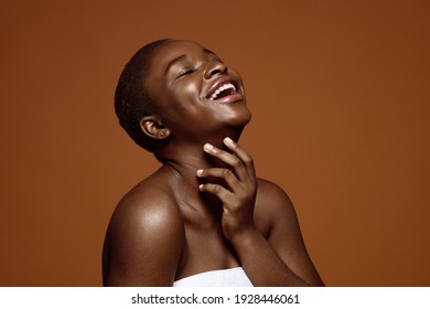 Essential Beauty. Joyful black woman with short hair touching her soft flawless skin on neck, attractive african american lady enjoying result of beauty treatments, standing over brown background