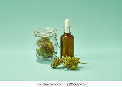 Essential cannabinoid oils bottle and glass jar with dry marijuana buds. Legalized drug and addiction. Herbal medicine and painkiller therapy. Natural organic cannabis. Green background. Copy space