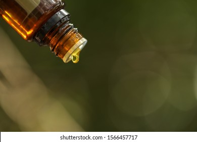 Essential Oil Bottle Close Up With Drop Of Oil Forming. Bokeh Background Provides Copy Space.