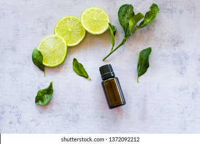 Essential oil bottle with lime & lime leaves on concrete bench - flat lay
