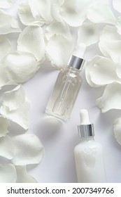 Essential Oil Bottles And Rose Petals On White Background. Flat Lay, Top View.