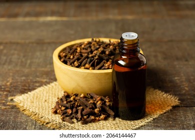 Essential oil of cloves in bottle and dry cloves on wooden bowl on rustic wooden background.