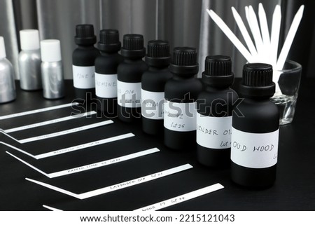 essential oil and frangrance oil bottle on black wooden table with blotter paper for testing smell during blending process for choosing nice scent for making scented candles and body perfume in lab
