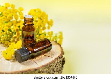 Essential oil of the medicinal herb tansy in a dark bottle with a lid on a wooden saw on a yellow background. Space for text. Aromatherapy, spa, skin care.