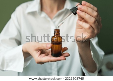 Essential oil with a pipette in the hands of a woman on a green background. Women's hands with a bottle of oil and a pipette - the sphere of beauty