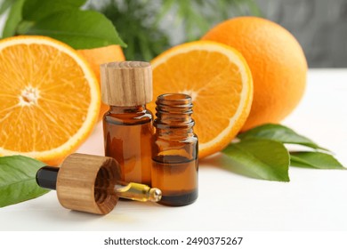 Essential oils in bottles, dropper, oranges and green leaves on white table
