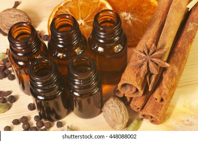 Essential Oils In Glass Bottles And Spices (anise, Nutmeg, Cardamon, Cinnamon, Clove, Pepper) On Wooden Background. Overhead View