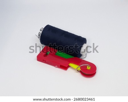 Essential sewing tools, a spool of dark thread and a vibrant cutter, stand ready for your next creative project on a clean white background