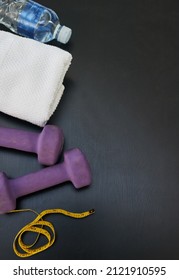 Essentials For Your Gym Bag. High Angle Shot Of A Water Bottle, Towel, Weights And Tape Measure Against A Black Background.