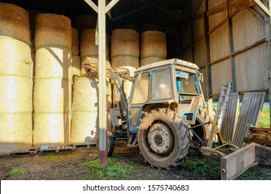 Essex, UK - Circa November 2019: Farmer Seen In His Tractor, About To Pick Up A Very Large And Heavy Round Hay Bale Using A Fork At The Front Of His Tractor. Part Of A Rural Dairy Farm In The UK.