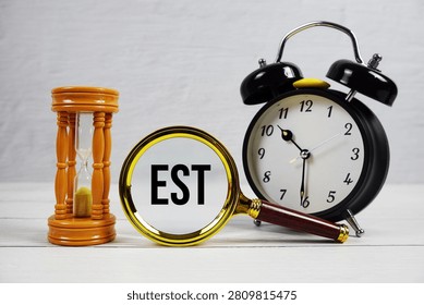 EST Earliest Starting Time text with alarm clock on wooden background