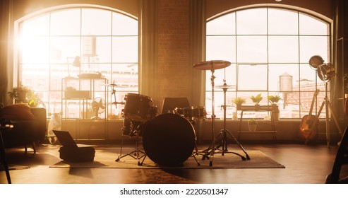 Establishing Shot: Music Rehearsal Studio in Loft Room with Drum Set in the Middle of It. Stylish Interior with Two Big Windows, Cozy Sofa, Shelves and Plants. Sunny Bright Day and Urban City View.