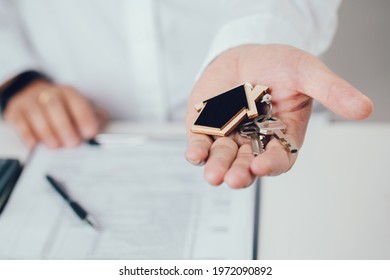 Estate agent hand holding house keys  with house shaped keychain. Mortgage concept. Real estate, moving home or renting property. - Shutterstock ID 1972090892