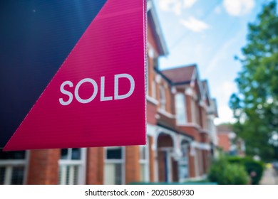 Estate agent SOLD sign with defocussed street of houses in background