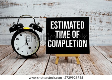 Estimated Time Of Completion text with easel and alarm clock on wooden background