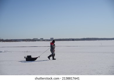 Pärnu Estonia - March 20 2022: Man In Very Warm Clothes Walking Over The Sea Ice To The Free Water. Fisherman With His Equipment On The Small Sledge Going Fishing. Baltic Sea, Pärnu Gulf.