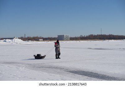 Pärnu Estonia - March 20 2022: Man In Very Warm Clothes Walking Over The Sea Ice To The Free Water. Fisherman With His Equipment On The Small Sledge Going Fishing. Baltic Sea, Pärnu Gulf.