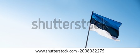 Estonian flag waving in wind and sunlight. Flag of Estonia on blue sky background. Empty copy space for text.