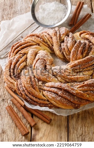 Estonian Kringle Cinnamon Braid Bread with powdered sugar closeup on the paper on the wooden table. Vertical