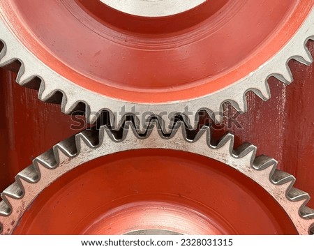 etail of two gearswheel of a machine on a red background, detail of case hardening, precision mechanics, gearing, two gears meshing together, horizontal