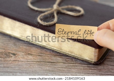 Eternal life, a handwritten text note and a closed Holy Bible Book with golden pages and a vintage ribbon on a wooden table. The gift of salvation and new life from God Jesus Christ, biblical concept.