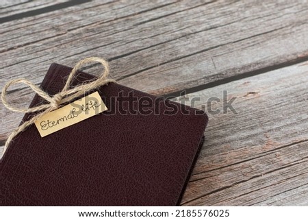 Eternal life, handwritten text on a small note placed on a closed Holy Bible Book wrapped with vintage ribbon on a wooden table. Christian biblical concept.