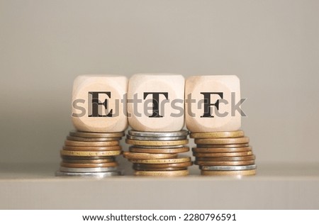 ETF abbreviation for Exchange Traded Fund written on wooden dice lying on piles of coins. Close-up photo.
