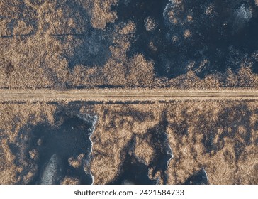 Ethereal aerial view captures a small road winding through frozen marshlands. Nature's frosty touch transforms the landscape, creating a serene winter scene. - Powered by Shutterstock