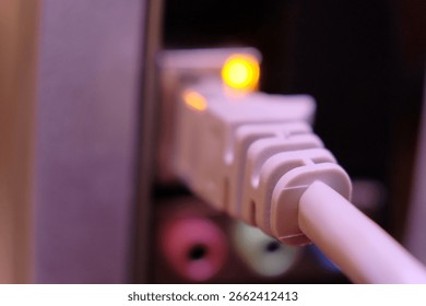 Ethernet cable connector partially inserted into a port. The connector features a glowing yellow LED indicator, signaling active network connection highlights additional ports and cables