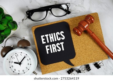 Ethics First text on speech bubble with alarm clock and wooden gavel on marble background
