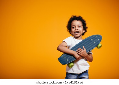 Ethiopian Boy in a white T-shirt and jeans hugs a skateboard and presses it to his chest on orange background - Shutterstock ID 1754181956