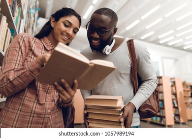 Ethnic indian mixed race girl and black guy surrounded by books in library. Students are looking for books.