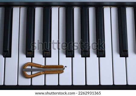Ethnic jew's harp lies on the piano keys. Close up top view of musical instruments. The concept of the characteristics of the cultures of the West and East. A mixture of genre and style.