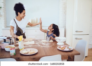 Ethnic Joyful Woman And Excited Adorable Daughter Enjoying Cooking Together And Giving High Five Near Messy Kitchen Table At Home