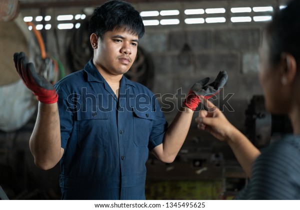 Ethnic mechanic recieving a scolding from an\
angry customer - Repair technician told off from an unhappy client\
in the garage repair\
workshop