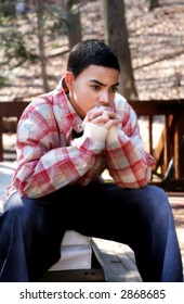 Ethnic mixed teen boy wearing casual clothing deep in thought in outdoor setting