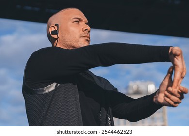 Ethnic serious sportsman in black jacket stretching on sunny day listening to music on blurred urban background with blue sky - Powered by Shutterstock