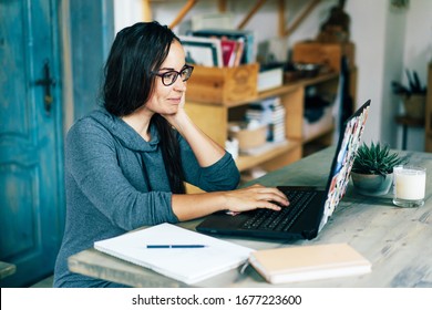 Ethnic simpotic dark-skinned brunette woman working on a laptop in the interior of a cozy living room or kitchen of her apartment. Remote work from home. Individual quarantine isolation.