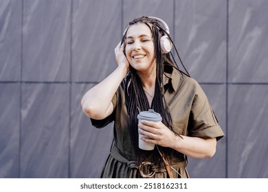 Ethnicity mid adult Armenian woman drinking coffee to go and having fun with music outdoors over grey wall . People, middle age, fun and active lifestyle concept. - Powered by Shutterstock