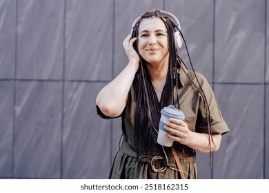 Ethnicity mid adult armenian woman drinking coffee to go and having fun with music outdoors over grey wall . People, middle age, fun and active lifestyle concept. - Powered by Shutterstock