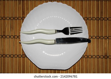Etiquette fork and knife on a white plate on a mat background