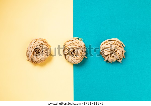 ettuccine : 3 nest of raw pasta on divided background\
yellow and light blue. Simple composition about italian quality\
pasta. 