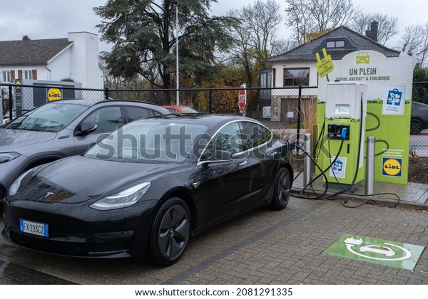 Eupen,\
Belgium - November 3, 2021: A static shot of a solid black Tesla\
Model 3 dual motor charging at the LIDL supermarket DC charging\
station in a rainy autumn day. Selective\
focus.