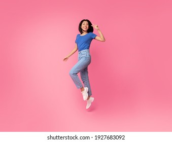 Euphoria Concept. Full Length Portrait On Energetic Young Asian Woman Jumping And Showing Victory V Sign Gesture With Two Fingers Isolated On Pink Studio Background. Excited Female Celebrating Win