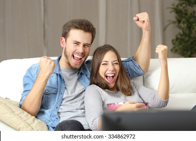 Euphoric Couple Watching Tv Sitting On A Couch At Home