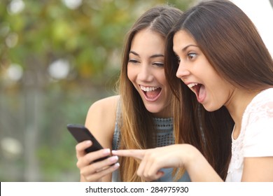 Euphoric friends watching videos on a smartphone and pointing at screen surprised