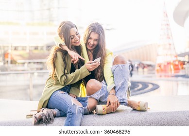Euphoric friends watching videos on a smartphone and pointing at screen surprised - Girlfriends laughing and having fun outdoors
