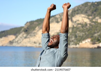 Euphoric man with black skin raising arms celebrating vacation on the beach - Shutterstock ID 2119075607