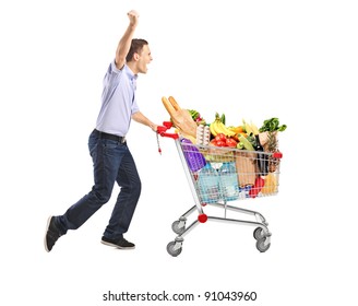 Euphoric Man Pushing A Shopping Cart Full With Food Isolated On White Background